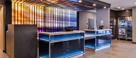 A modern reception area with a glass display case, a digital screen, and a refrigerator stocked with beverages.