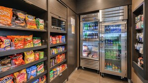 A snack and beverage vending area with multiple shelves stocked with various brands of chips and a refrigerator with a variety of drinks. - Fairfield Inn & Suites by Marriott Raleigh Cary (Cary)