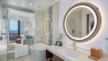 A modern bathroom with a glass shower enclosure, a large round mirror, and a bathtub.