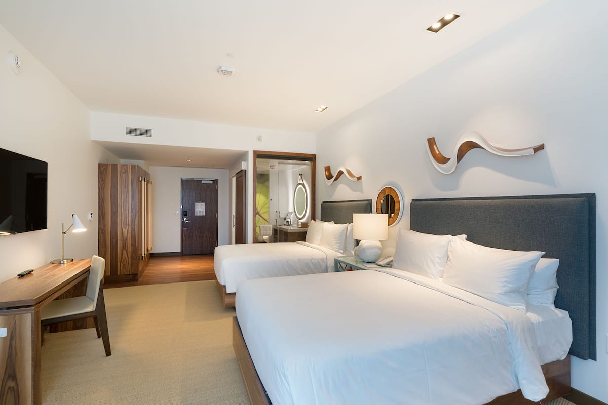 A hotel room with two beds, a desk, a chair, a TV, and a mirror.