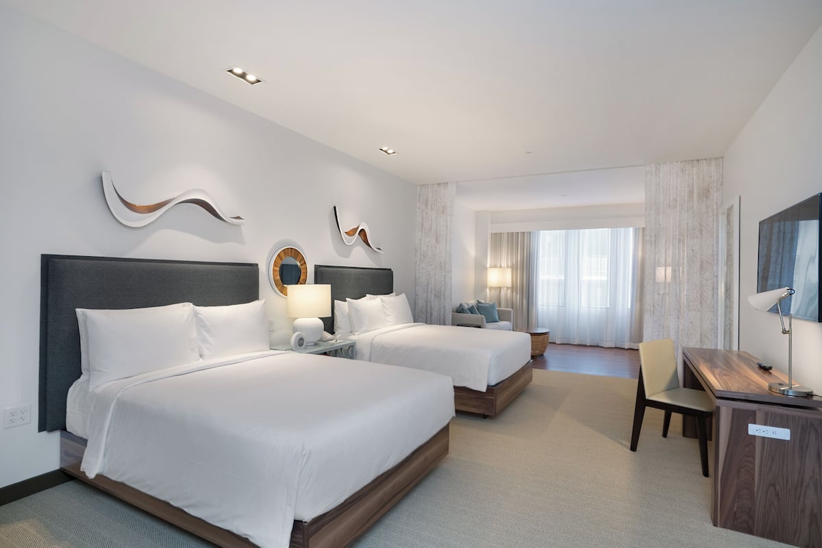 A hotel room with two beds, a desk, a chair, and a large window with curtains.
