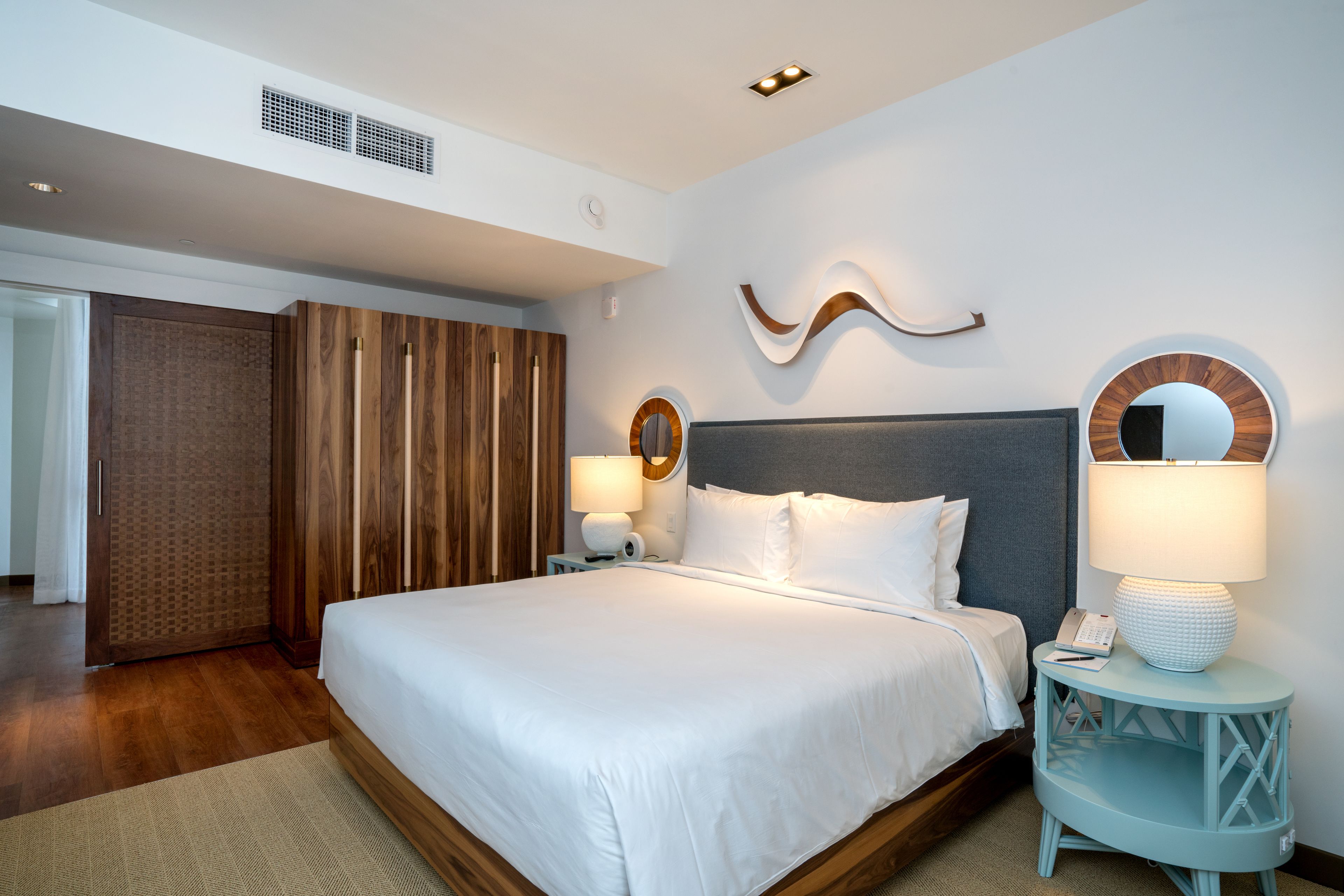 A modern hotel room with a large bed, wooden wardrobe, and a round mirror on the wall.
