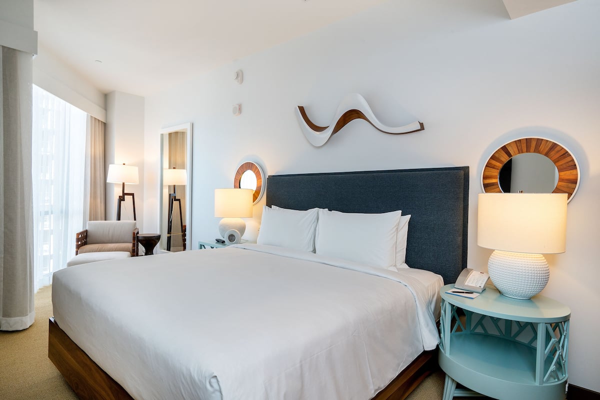 A hotel room with a large bed, two bedside tables, a chair, and a mirror.