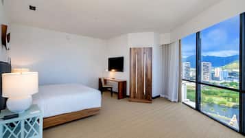 A hotel room with a bed, desk, and large windows offering a city view.