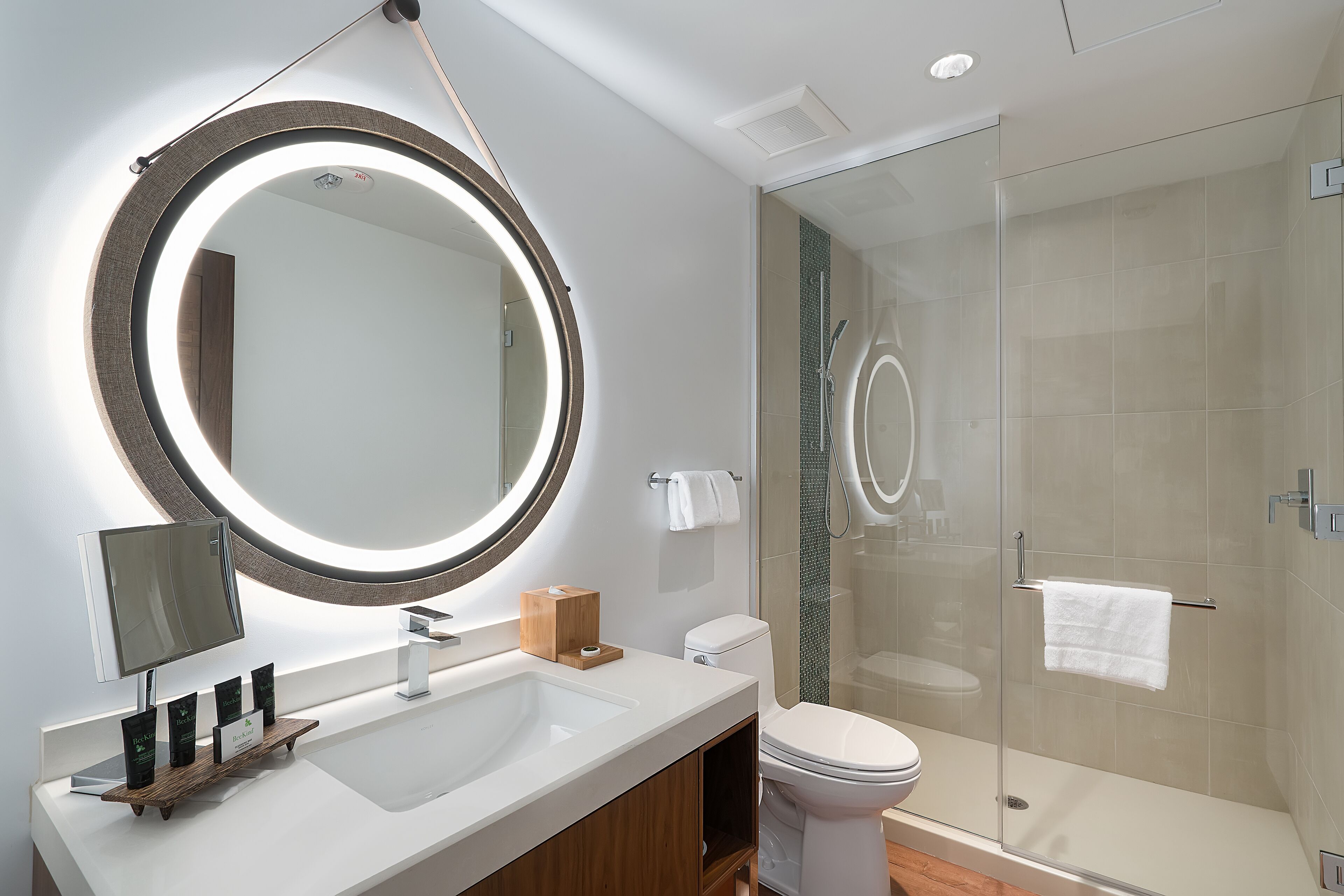 Un baño moderno con un espejo grande, un lavamanos, un inodoro y una ducha con mampara de vidrio.