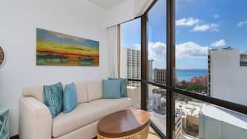 A modern living room with a large window, a beige sofa, and a colorful painting.