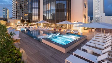 Área de piscina en la azotea con sillones de descanso y sombrillas, rodeada de edificios modernos.