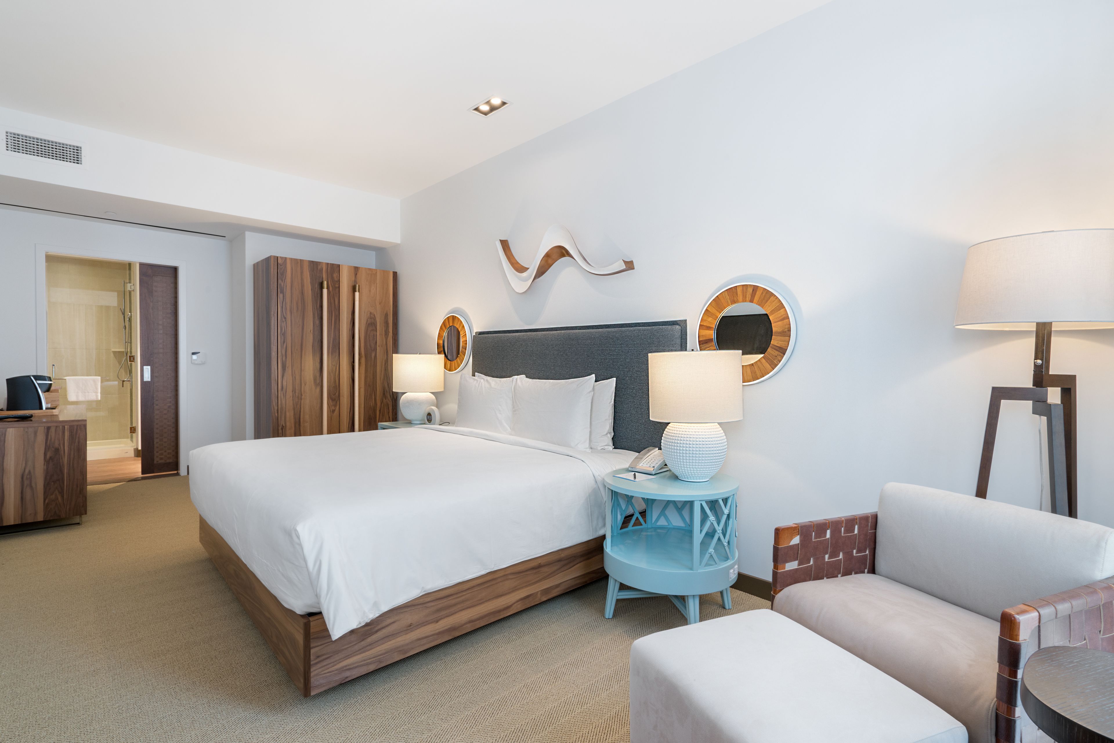 A hotel room with a large bed, two bedside tables with lamps, a chair, a desk with a computer, and a wardrobe.