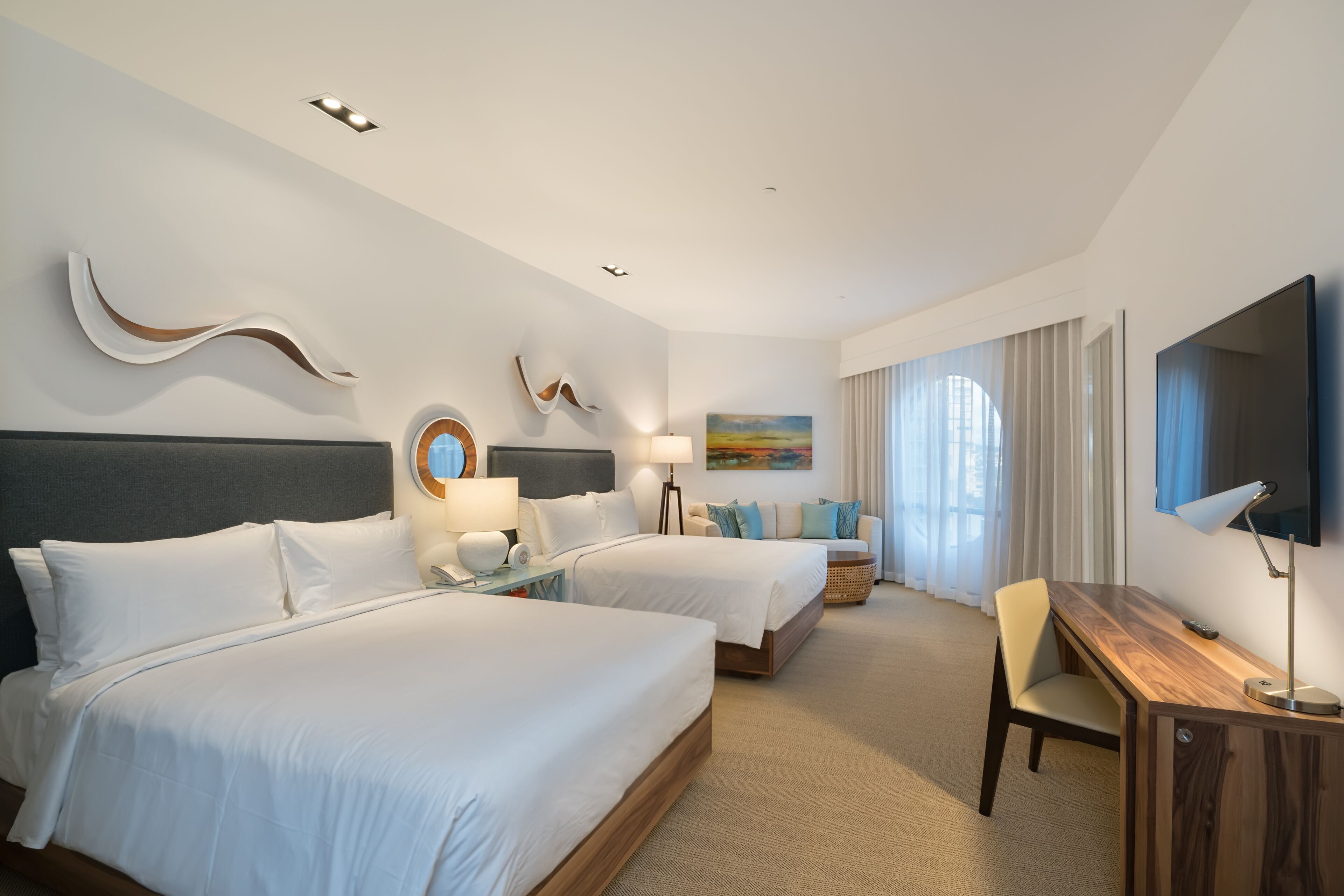 Een hotelkamer met twee bedden, een bureau, een televisie en een schilderij aan de muur.
