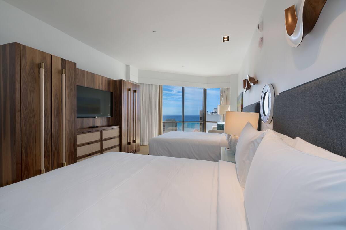 A hotel room with two beds, a TV, a large window with a view, and wooden paneling.