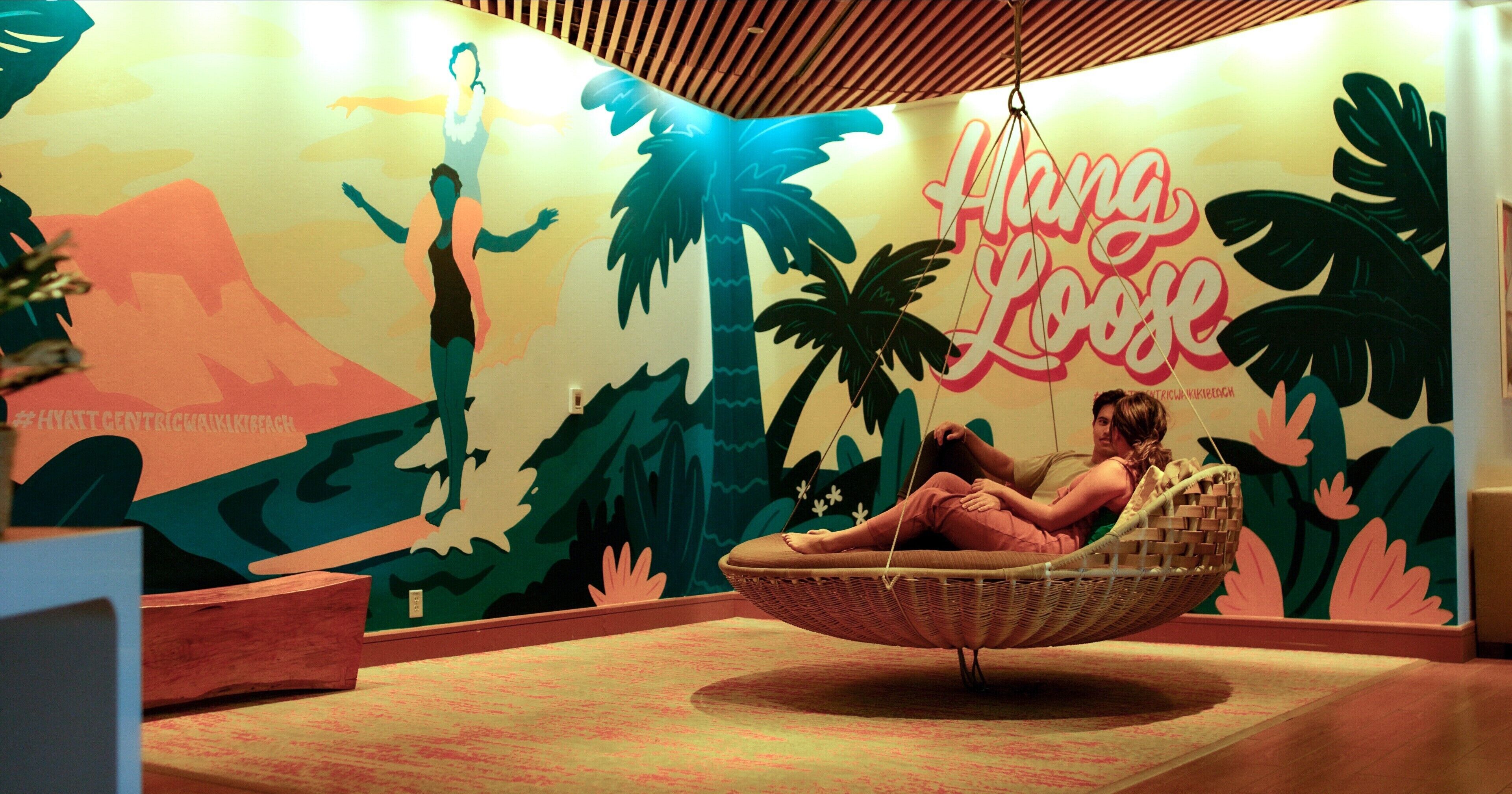 A room with a mural of tropical scenery and a hanging chair.