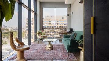 A modern living room with a large window, a green sofa, a wooden chair, and a patterned rug.