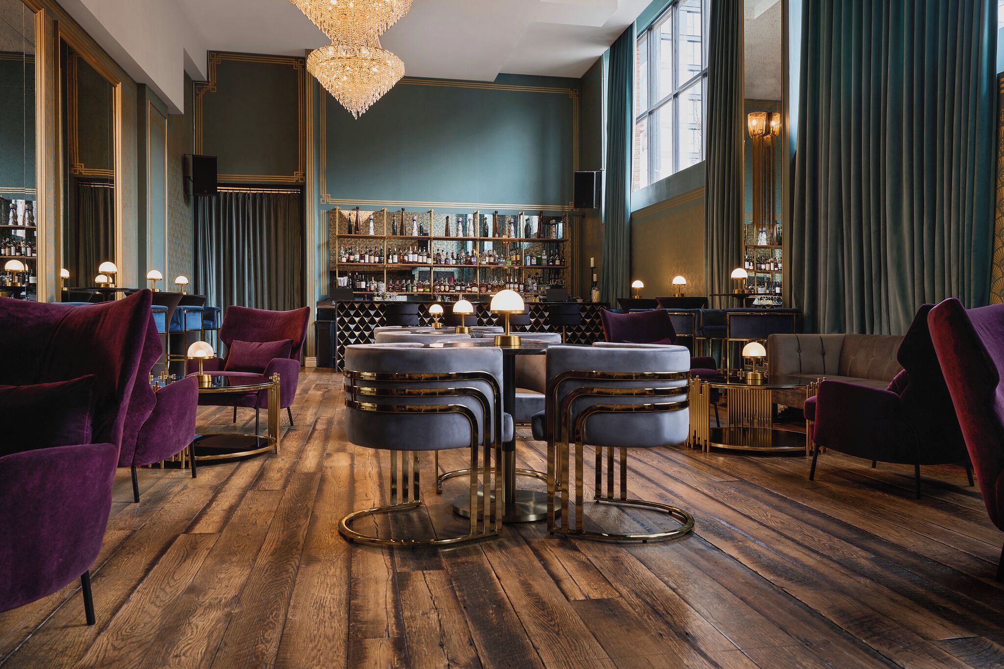 Zona de bar con suelo de madera, sillas de terciopelo morado y una barra con taburetes.