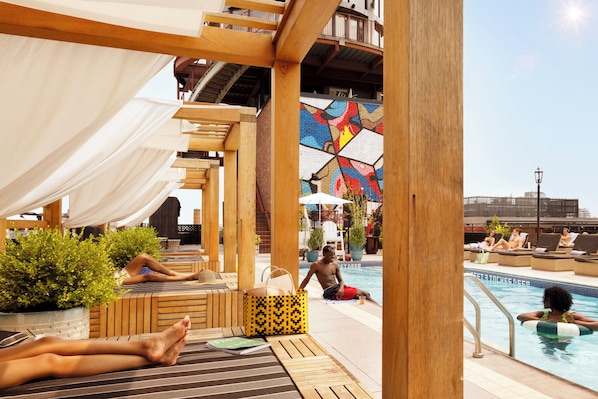 Zona de piscina con tumbonas de madera, una piscina y un mural.