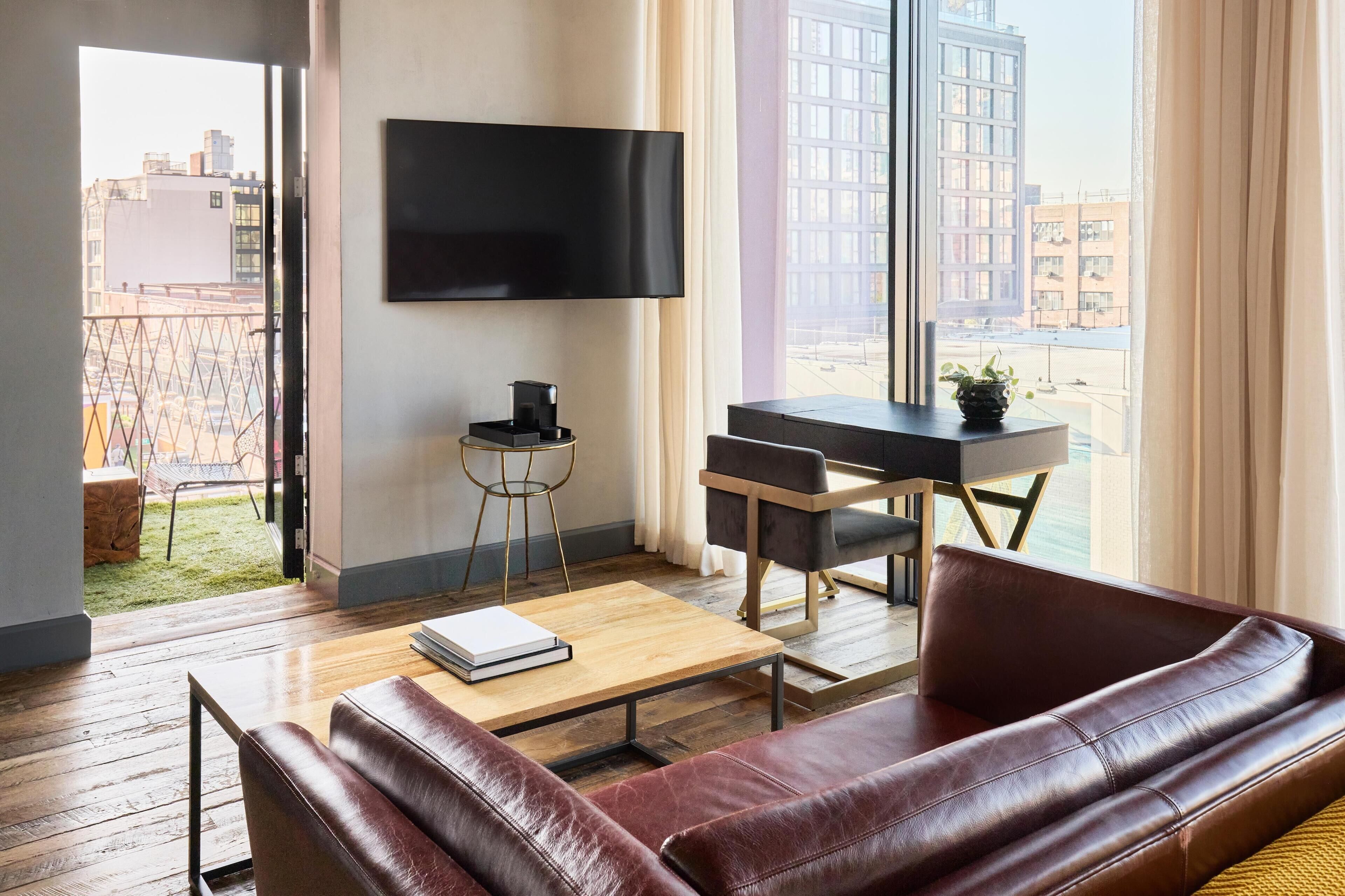 Una sala de estar moderna con un sofá de cuero, una mesa de centro, un televisor montado en la pared y un escritorio con una silla.