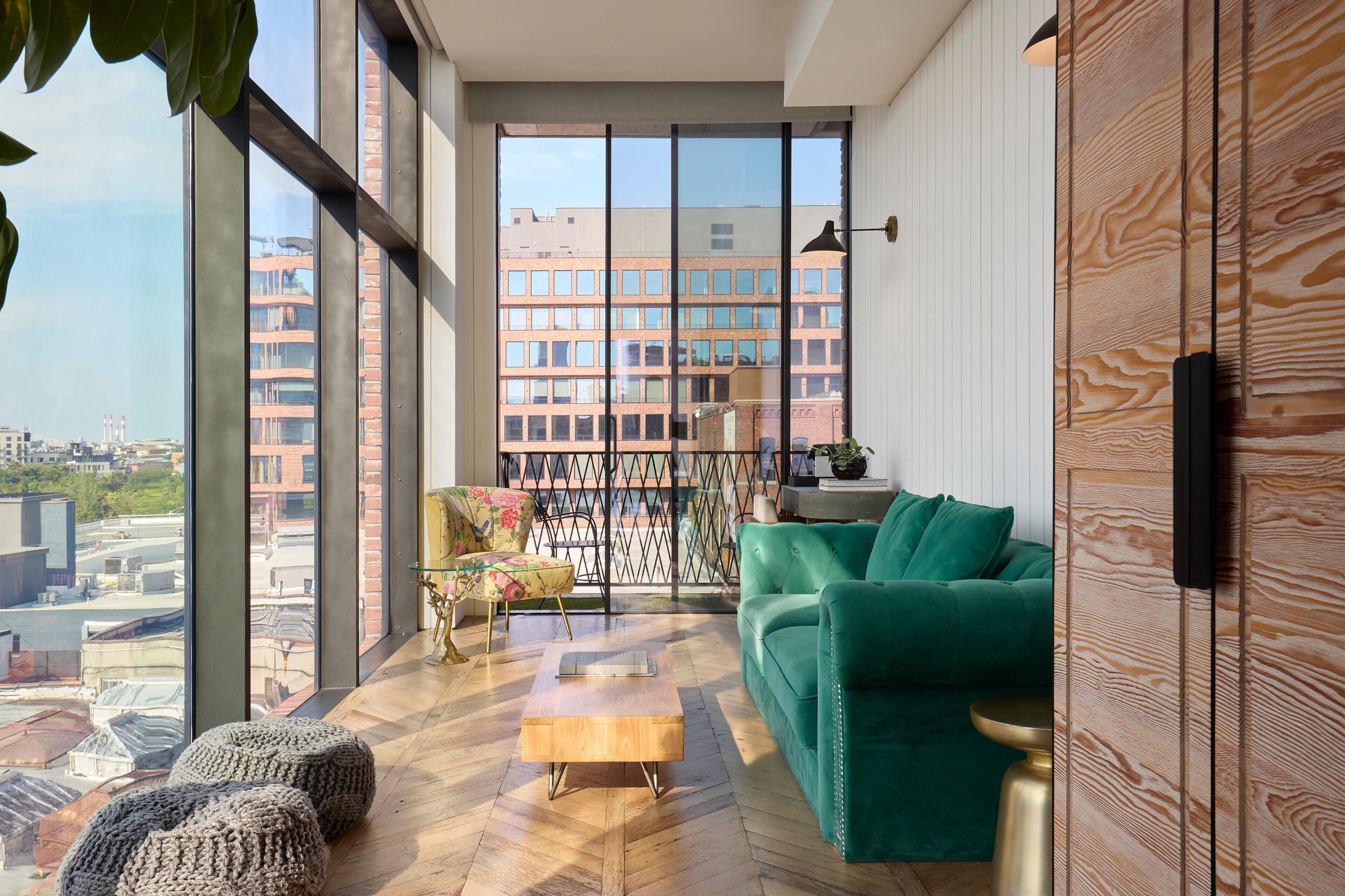 A modern living room with a green sofa, wooden coffee table, and large windows offering a city view.