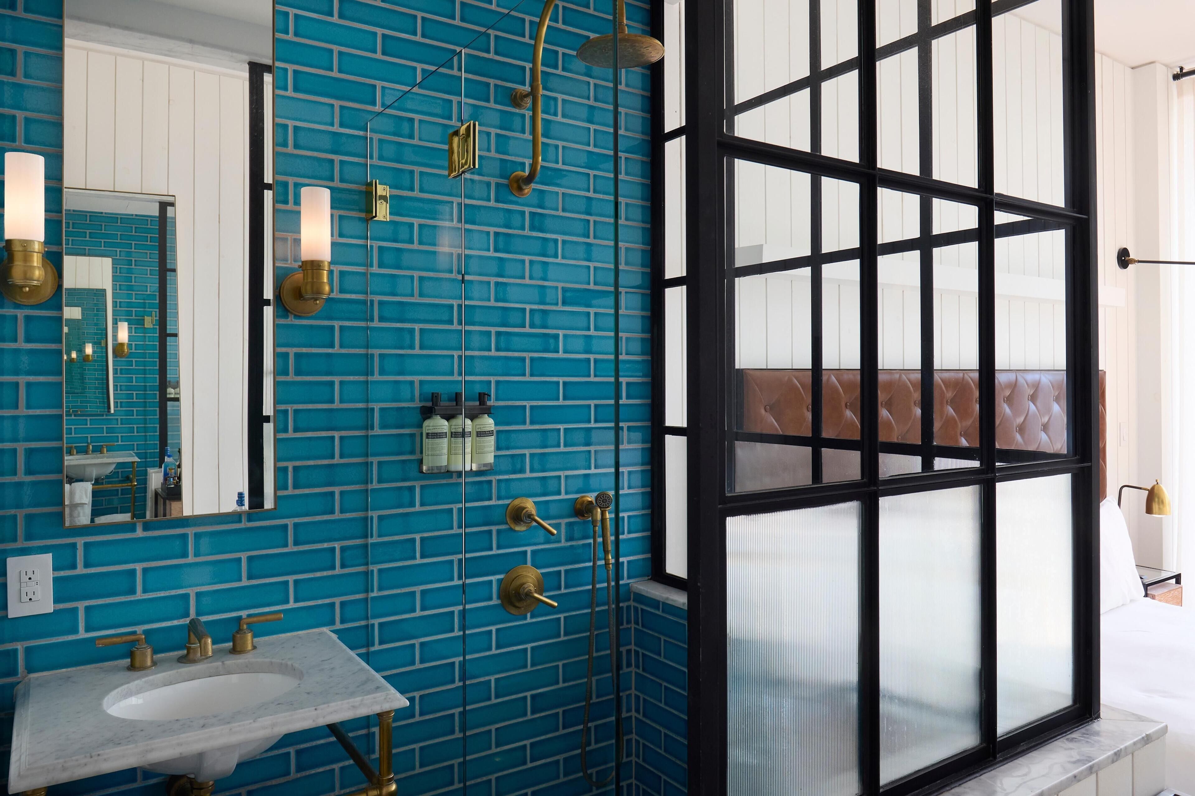 A bathroom with a blue tiled wall, a white sink, and a large window with a black frame.