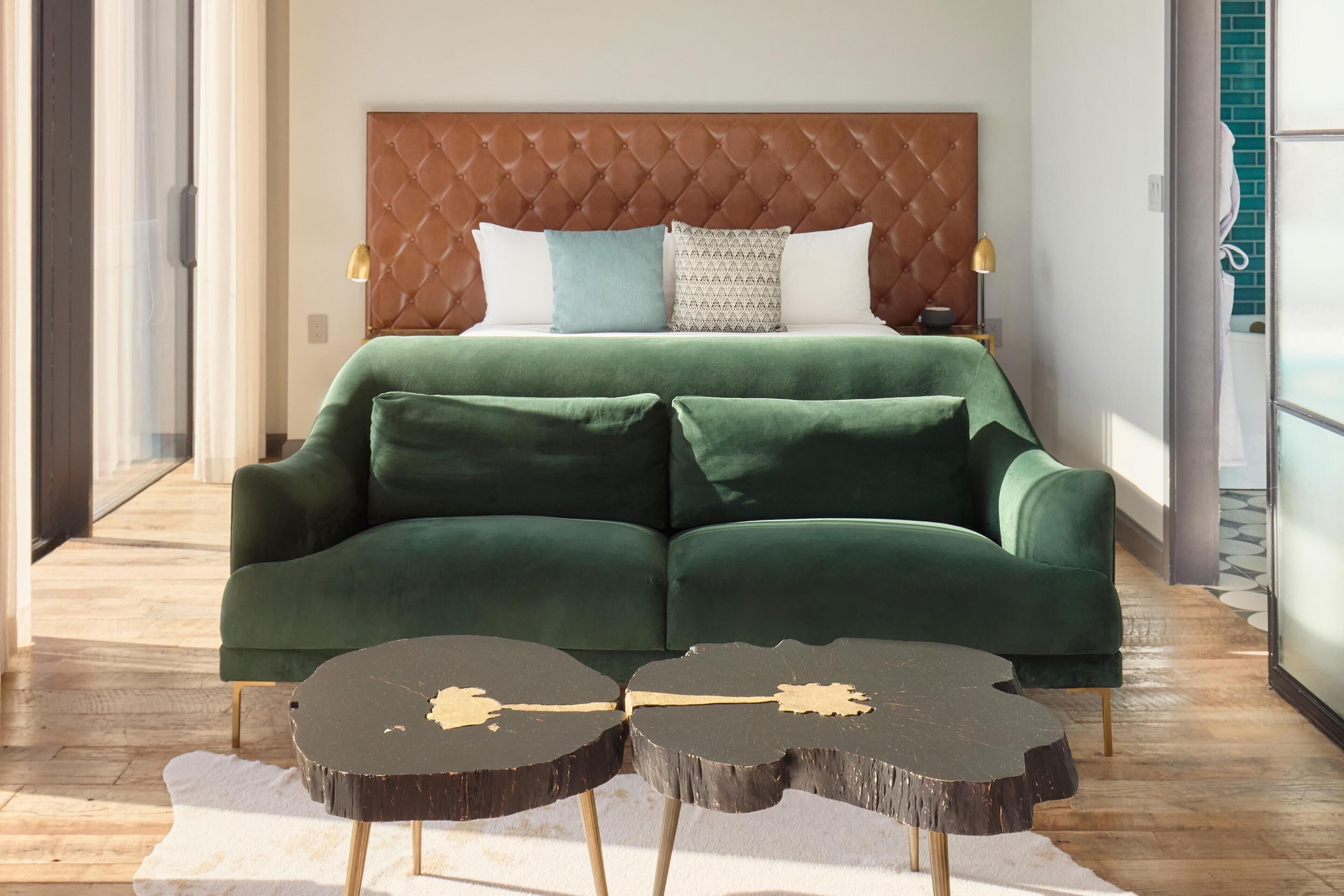Un dormitorio con cabecera capitonada, un sofá verde y una mesa de centro redonda de diseño original.