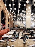 A restaurant with brick walls, hanging spherical lights, and a variety of seating arrangements including tables and booths.
