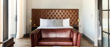 Habitación de hotel con una cama grande, un sofá de cuero, una mesa de centro de madera y una mesita de noche con lámpara.