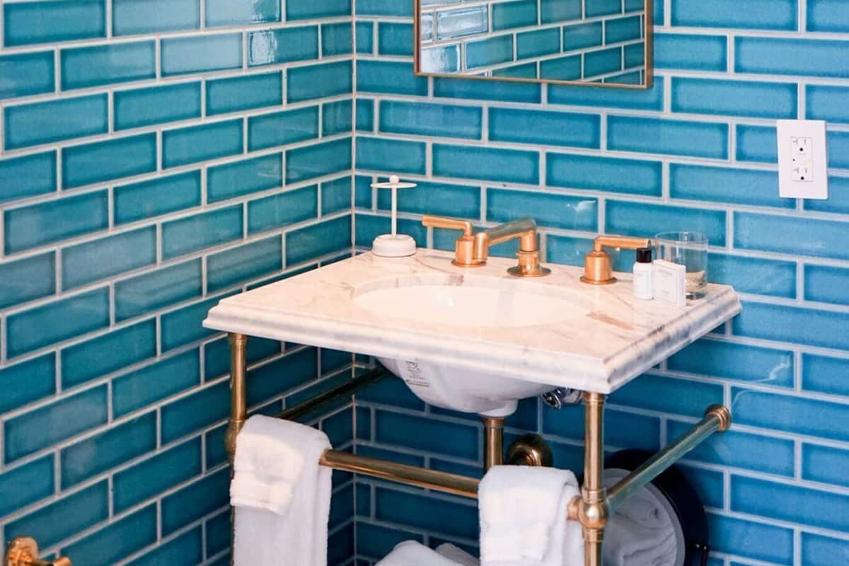 Une salle de bain avec un mur recouvert de carreaux bleus, un lavabo blanc doté de robinetterie dorée et un miroir au-dessus du lavabo.
