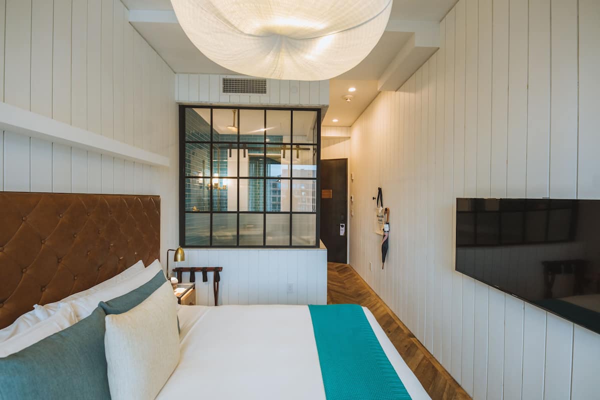 Une chambre d’hôtel moderne, dotée d’un grand lit, d’une télévision et offrant une vue sur la ville grâce à une grande fenêtre.