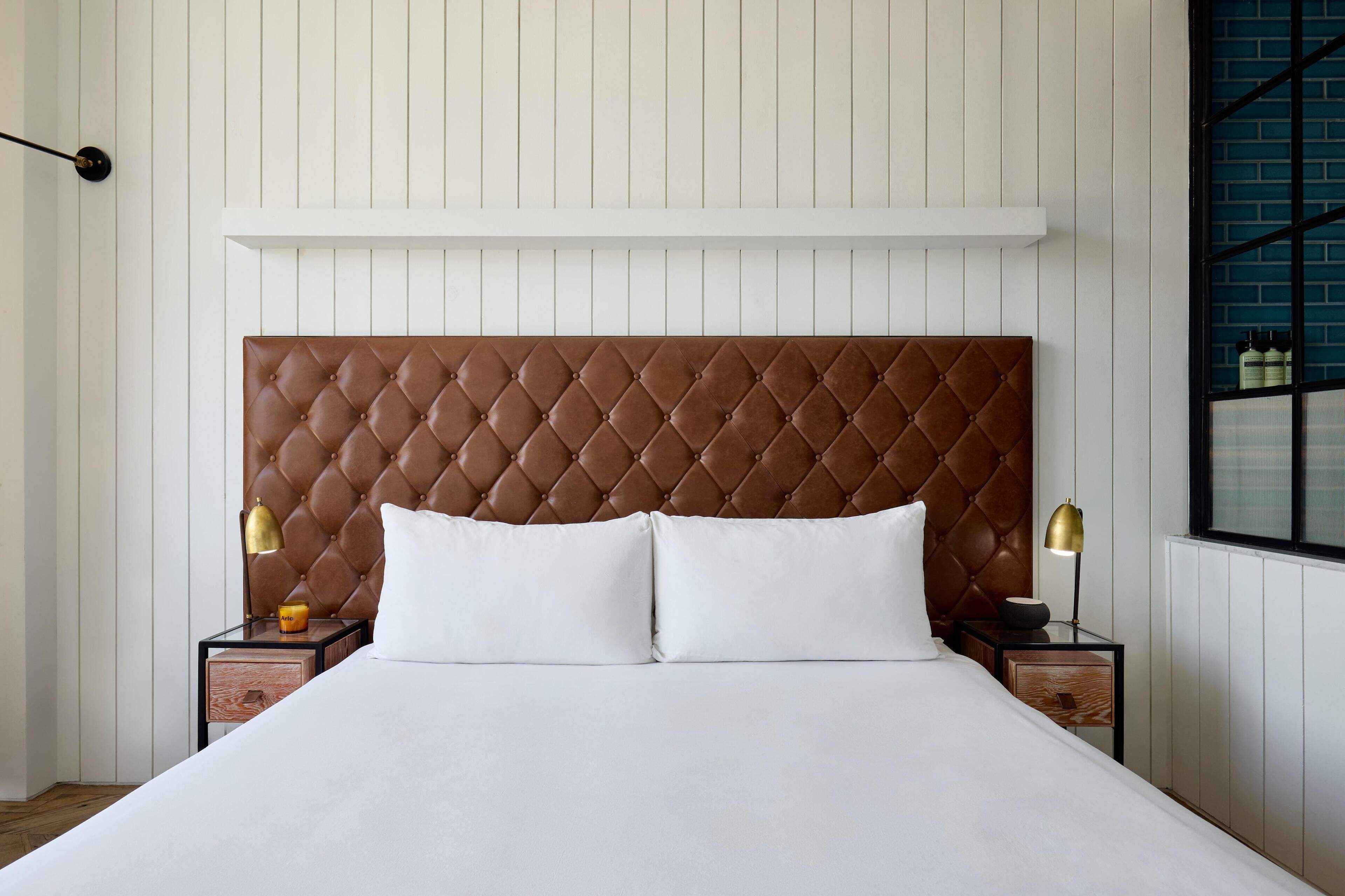 A bed with a tufted headboard, two bedside tables with lamps, and a window with a view of the outside.