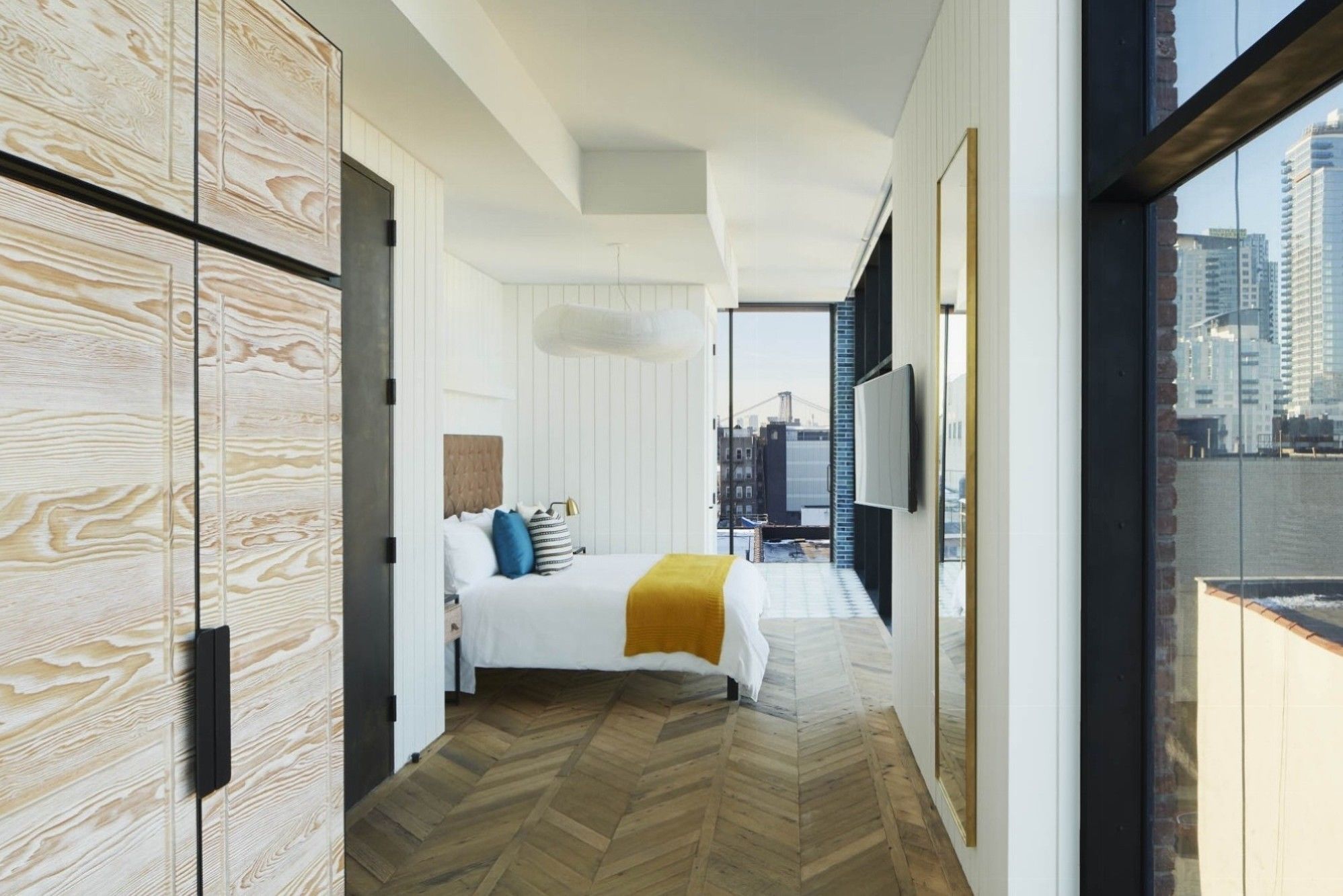 Quarto de hotel moderno com uma cama grande, vista para a cidade e piso de madeira.