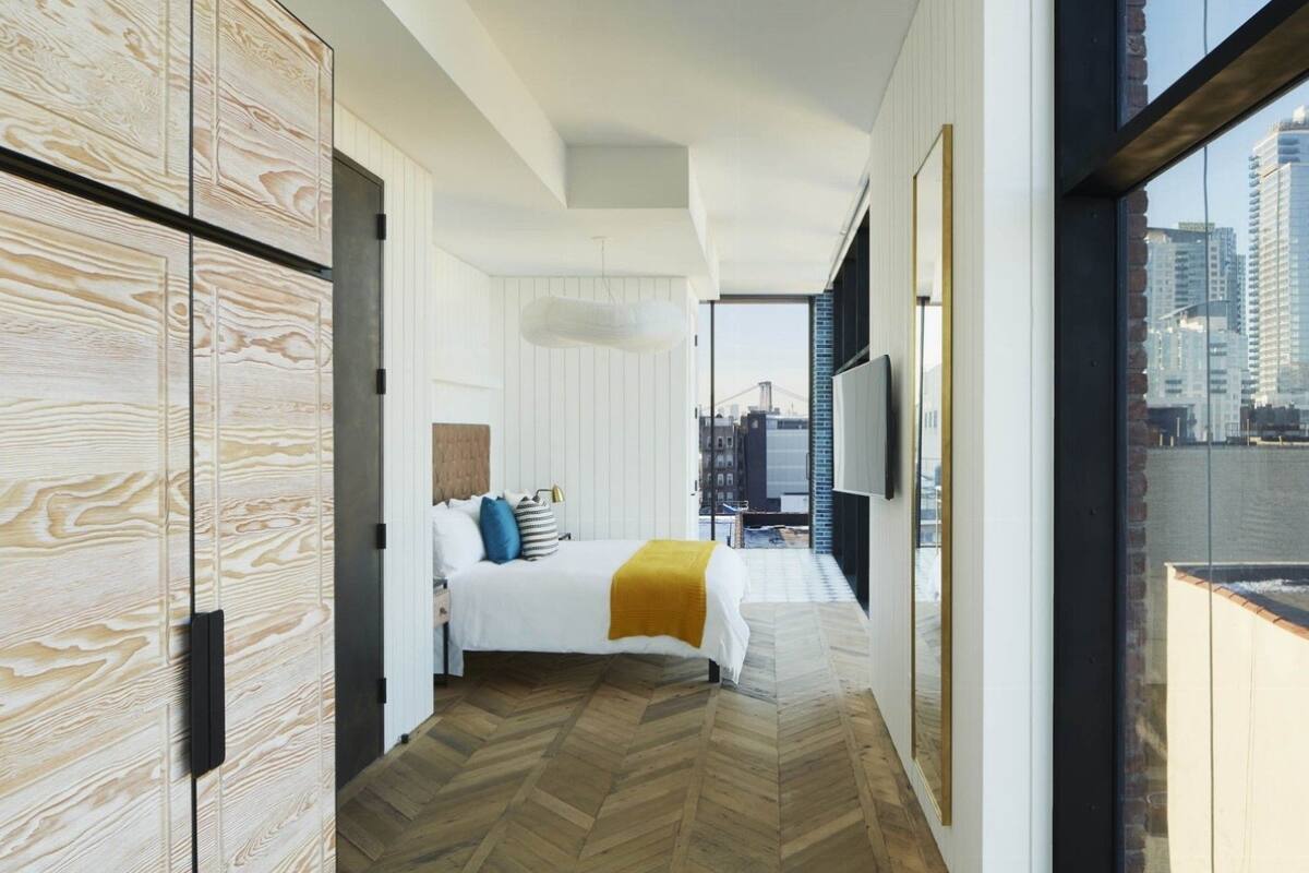 Una habitación de hotel moderna con una cama grande, vistas a la ciudad y suelo de madera.