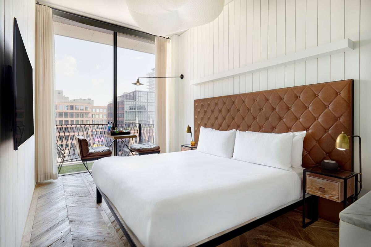 Une chambre d’hôtel avec un grand lit, un téléviseur fixé au mur, un balcon avec une chaise et une vue sur la ville.