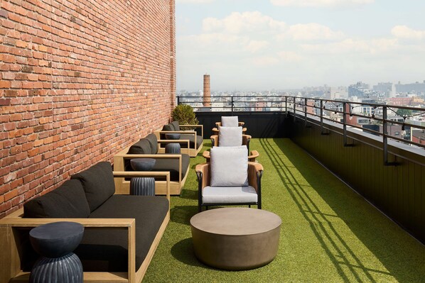Un salón en la azotea con pared de ladrillo, césped artificial verde y vistas a la ciudad.