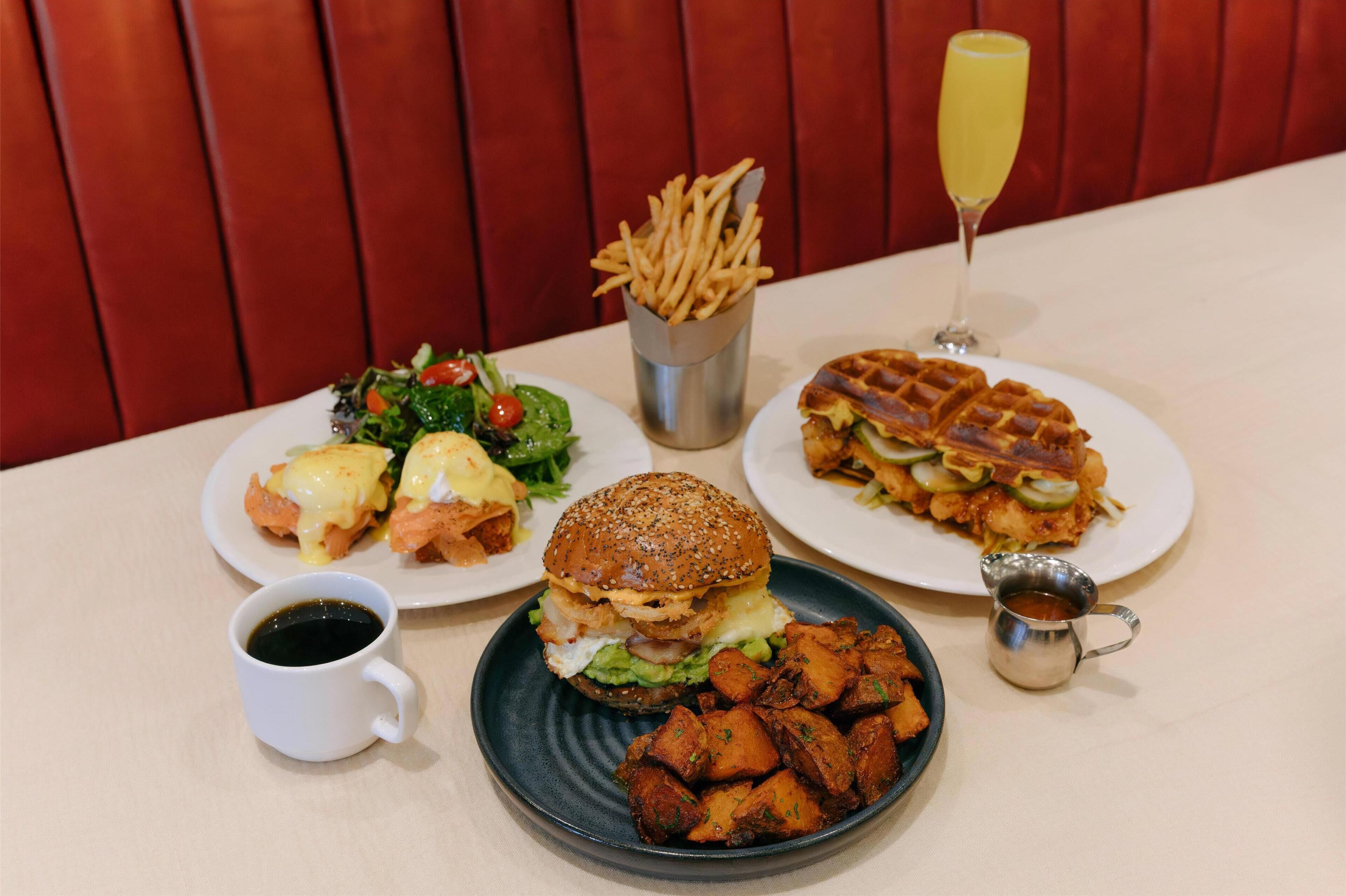 Una mesa con una variedad de platos, incluyendo una hamburguesa, papas fritas, una ensalada y un gofre.