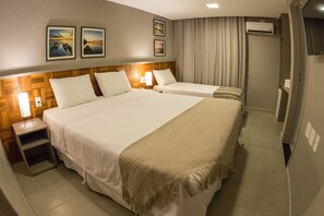 A hotel room with two beds, a wooden headboard, a nightstand with a lamp, and a wall-mounted air conditioner.