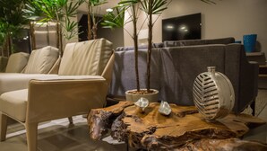 A modern living room with a sofa, a chair, a coffee table with decorative items, and a TV in the background. - Amenit Hotel (Maceió)