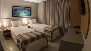 Une chambre d’hôtel avec deux lits, un téléviseur fixé au mur et une grande fenêtre avec des rideaux.