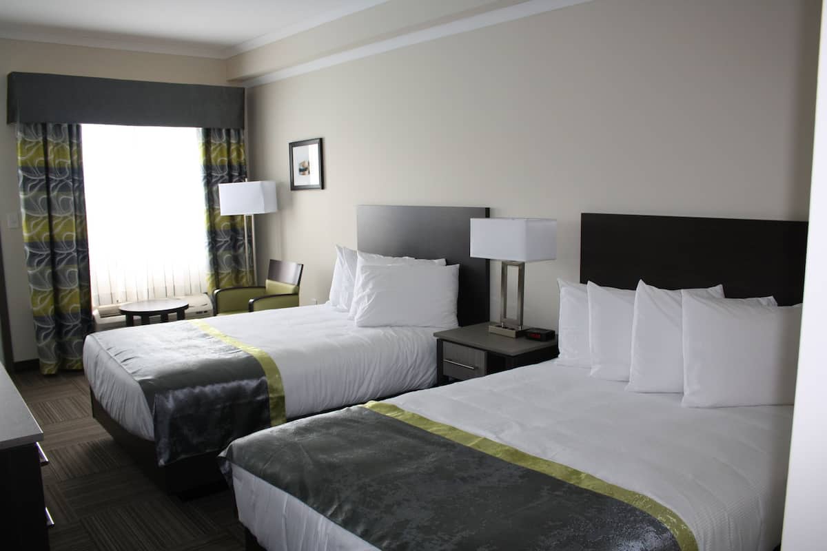 Habitación de hotel con dos camas, un escritorio, una silla y un ventanal con cortinas.