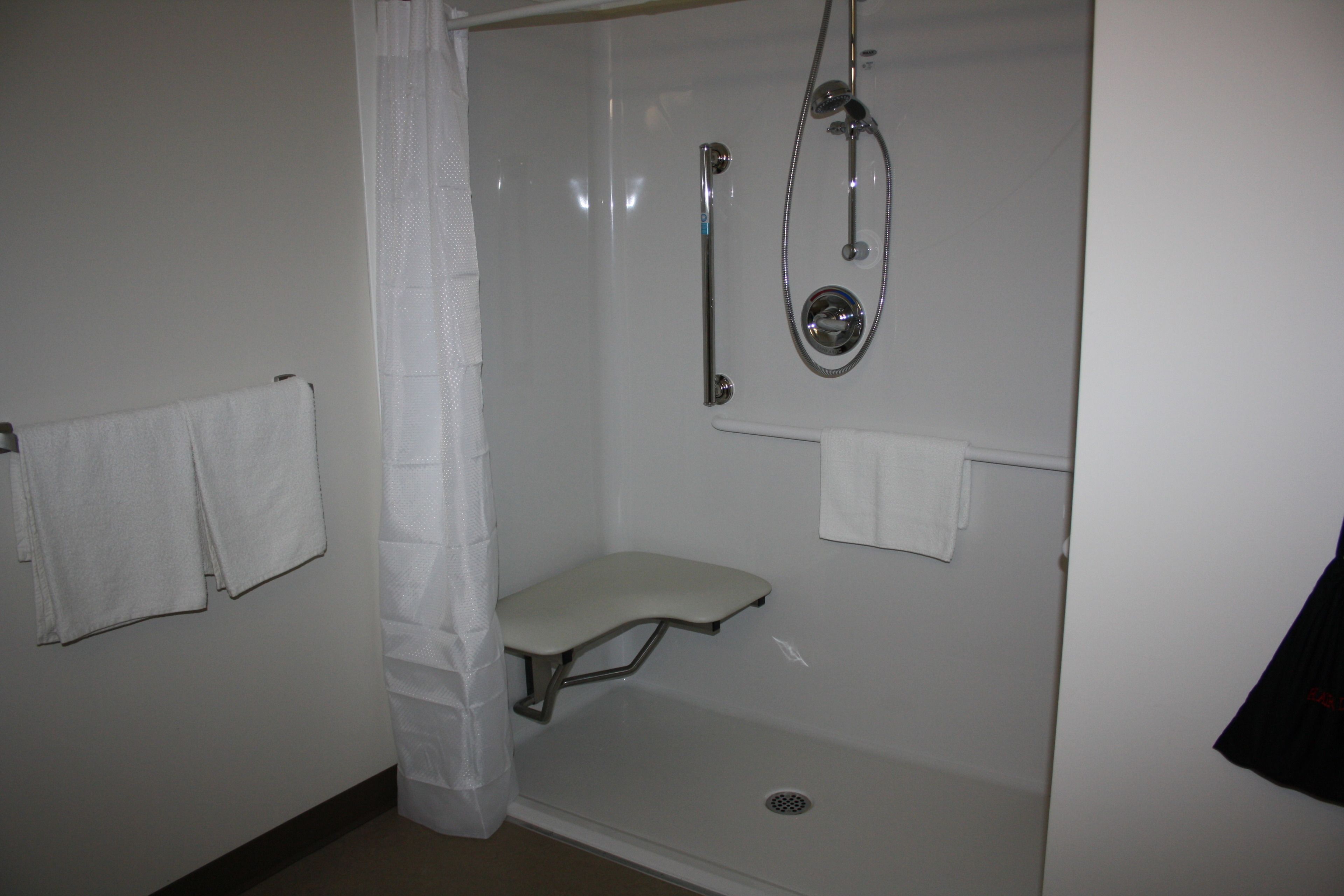 A small, enclosed shower area with a bench, a handheld showerhead, and a wall-mounted towel rack.
