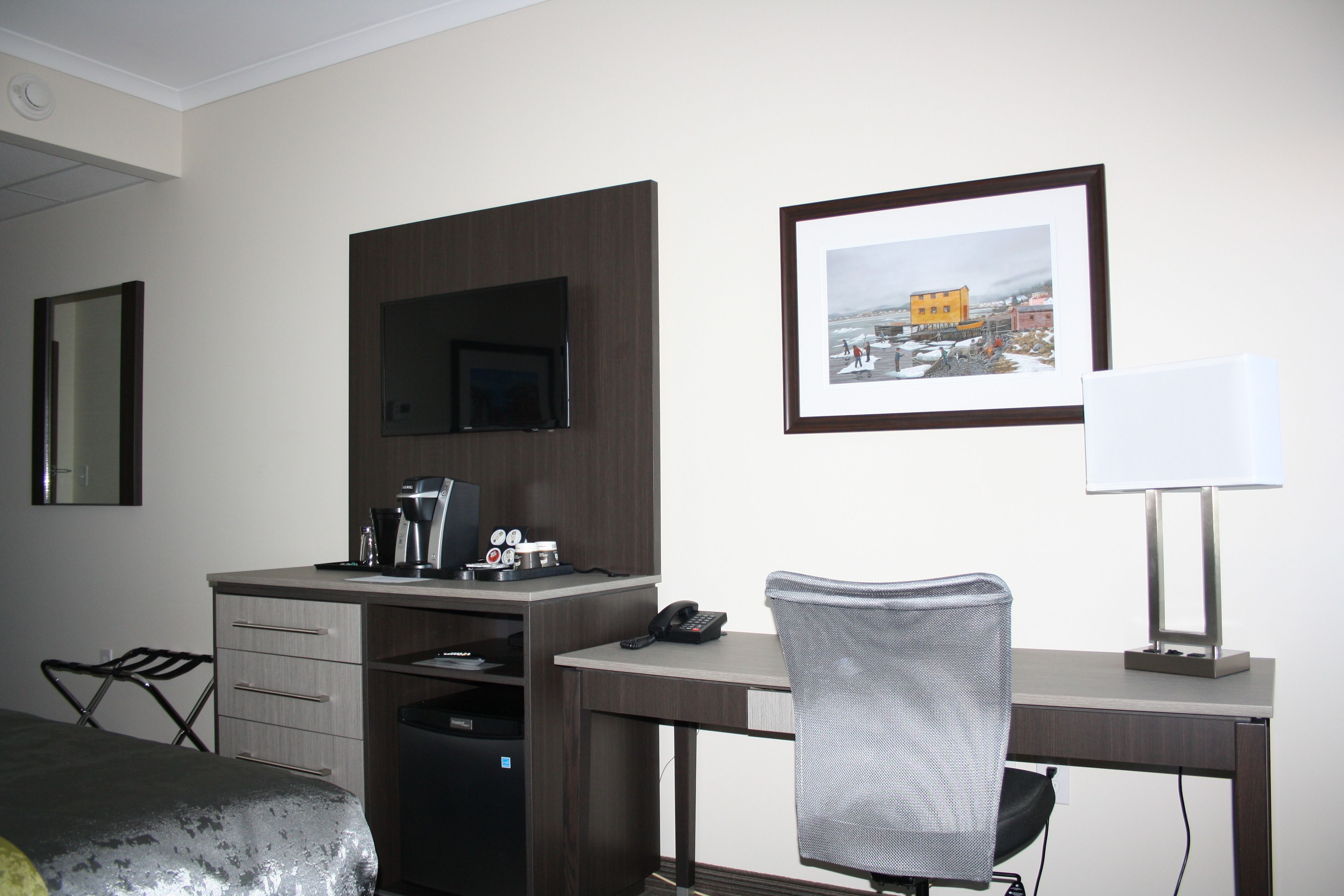 A hotel room with a desk, chair, bed, and a framed picture on the wall.