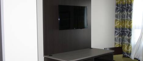 A modern room with a flat-screen TV mounted on a dark wood panel, a grey desk with drawers, and a green chair.
