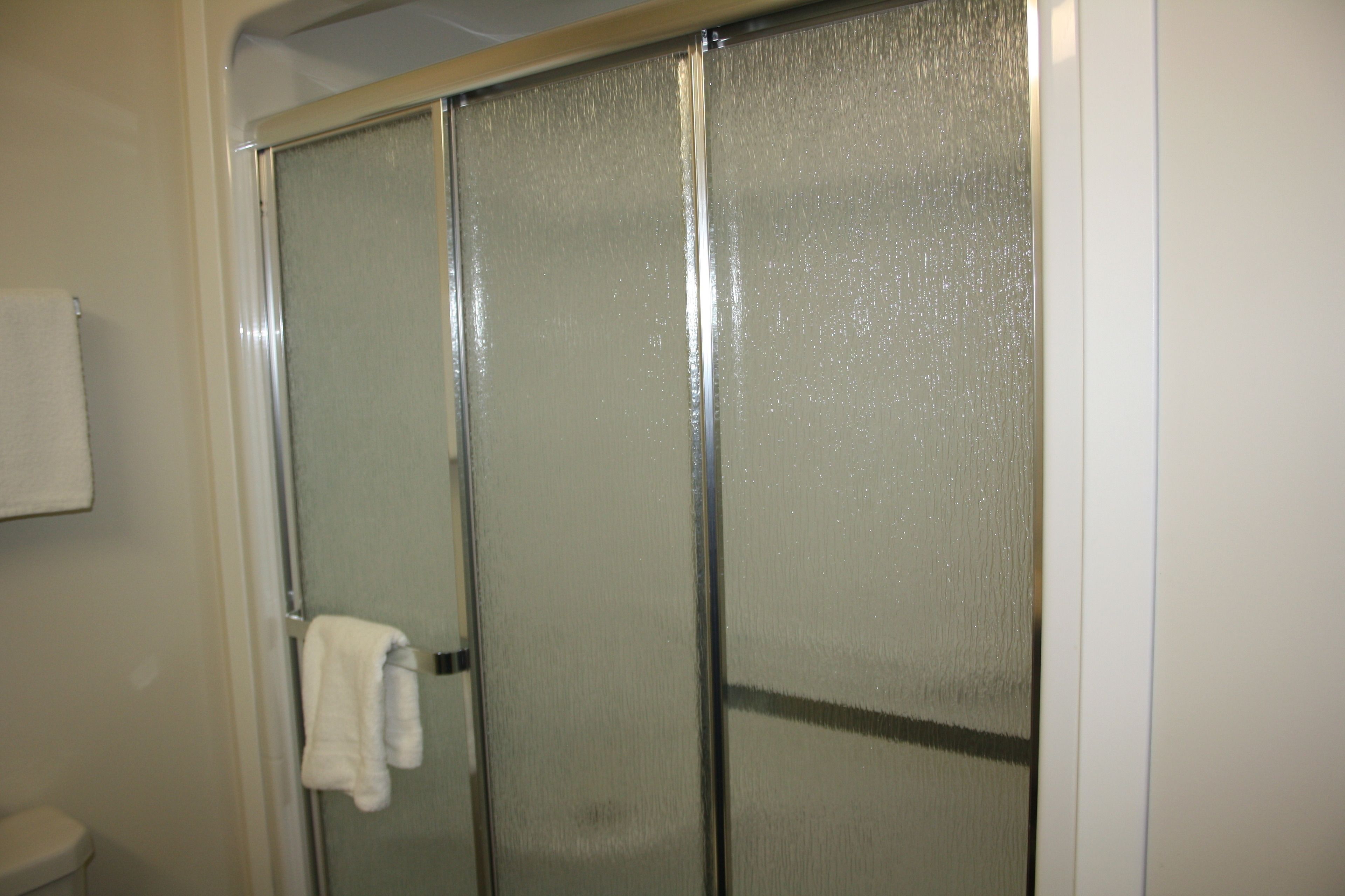 A bathroom with a glass shower enclosure, a white towel hanging on the door, and a white toilet.