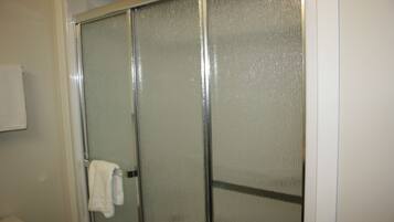 A bathroom with a glass shower enclosure, a white towel hanging on the door, and a white toilet.