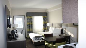 A hotel room with a bed, a desk, a chair, a TV, and a stove.
