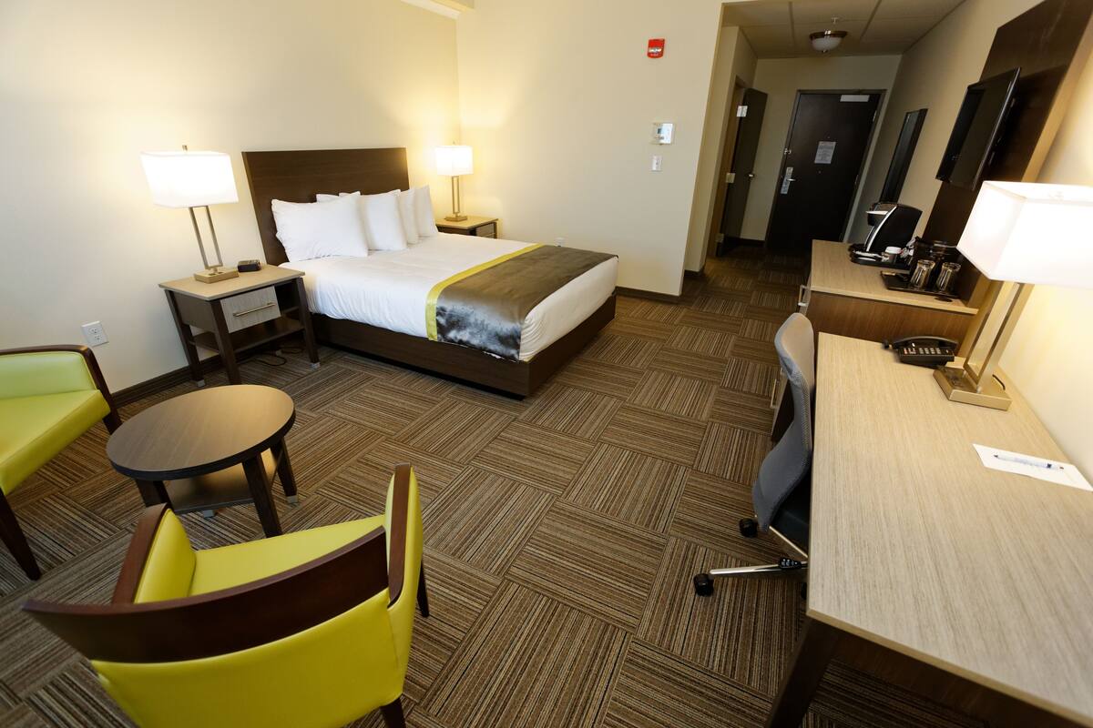 Habitación de hotel con una cama, dos mesitas de noche con lámparas, un escritorio con una silla y una pequeña mesa redonda.