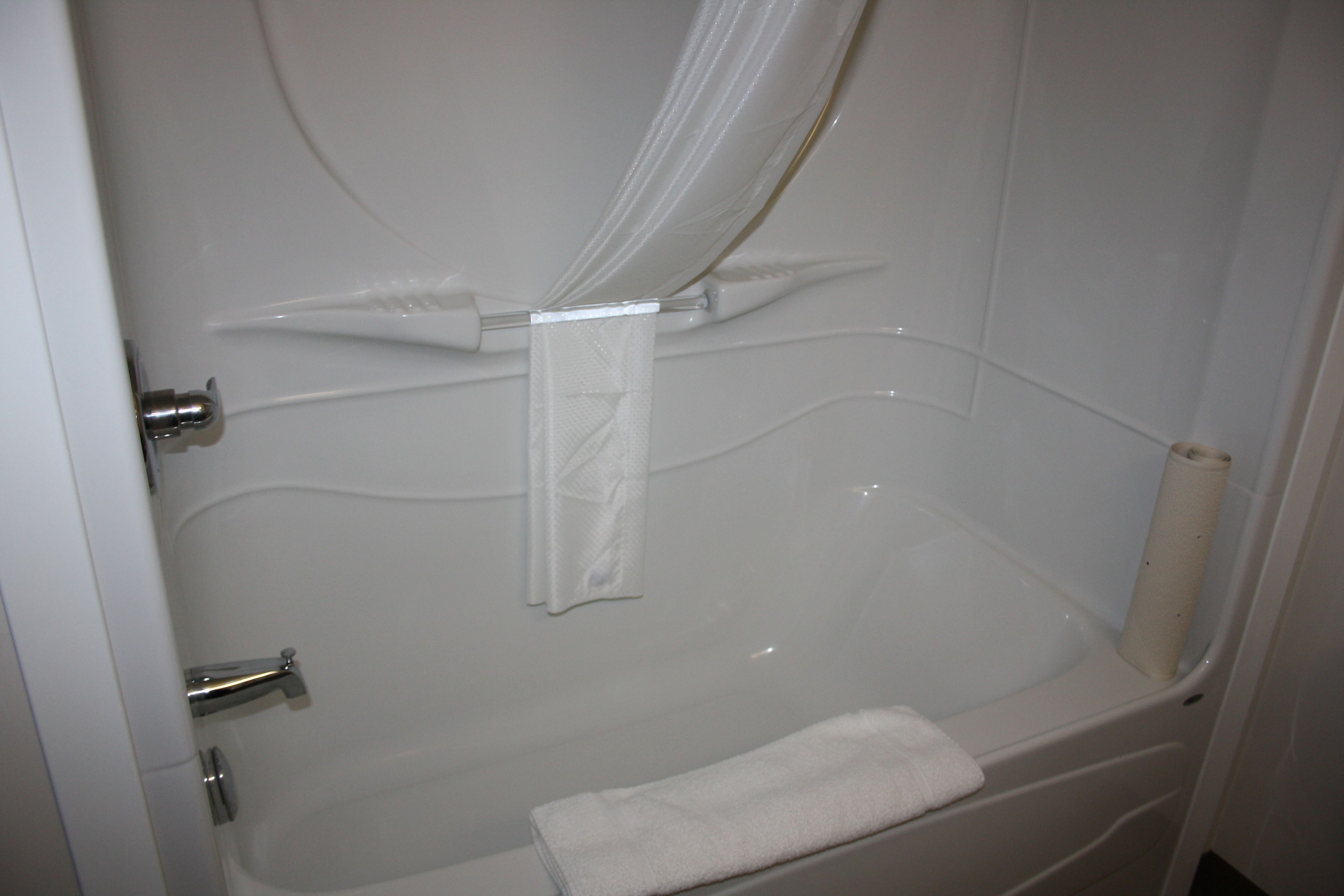 A bathroom with a bathtub, a shower curtain, and a towel on the floor.