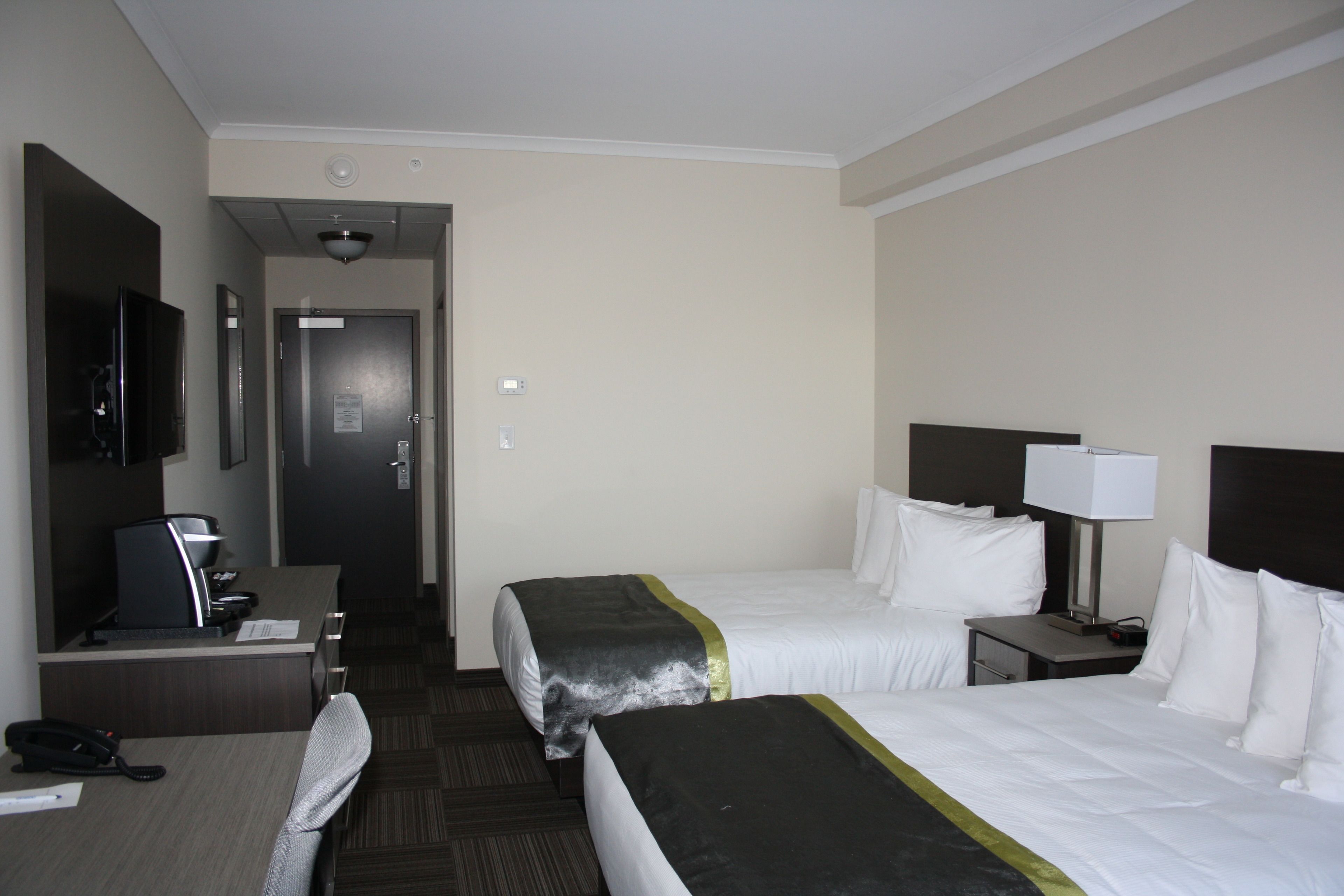 A hotel room with two beds, a desk with a computer, a telephone, and a television on the wall.