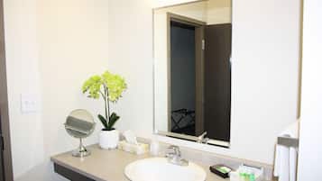Een badkamer met een wit wastafel, een spiegel, een potplant en toiletartikelen.