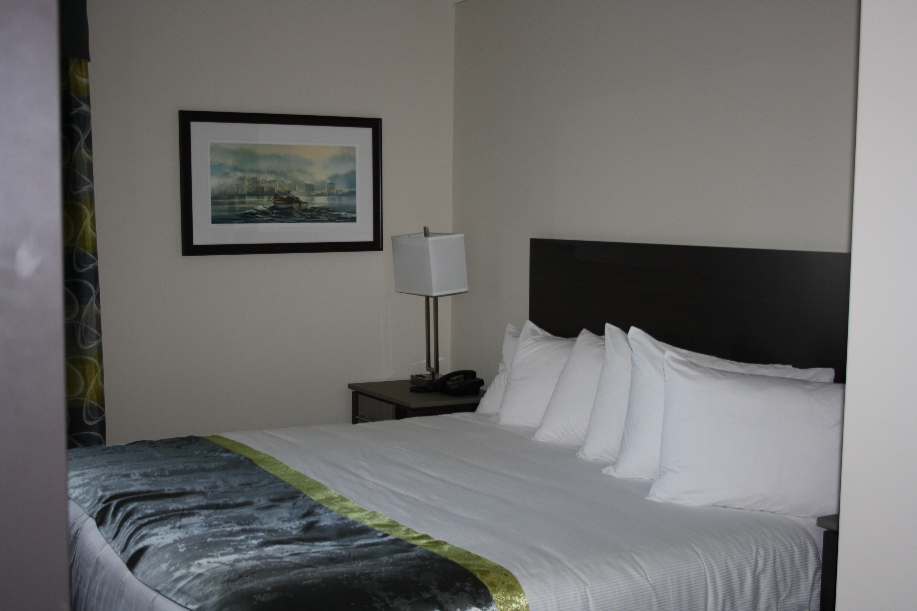 Una habitación de hotel con una cama bien hecha, un cuadro en la pared, una lámpara de noche y una mesita de noche.