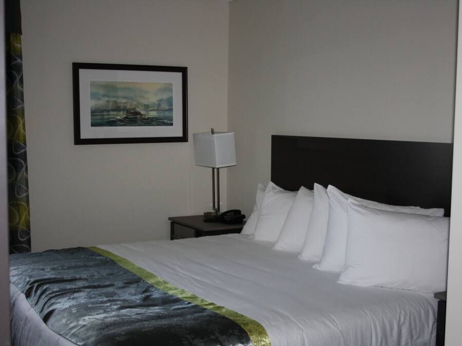 Una habitación de hotel con una cama bien hecha, un cuadro en la pared, una lámpara de noche y una mesita de noche.