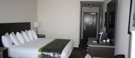 Habitación de hotel con una cama grande, un escritorio, teléfono, lámpara y cafetera.