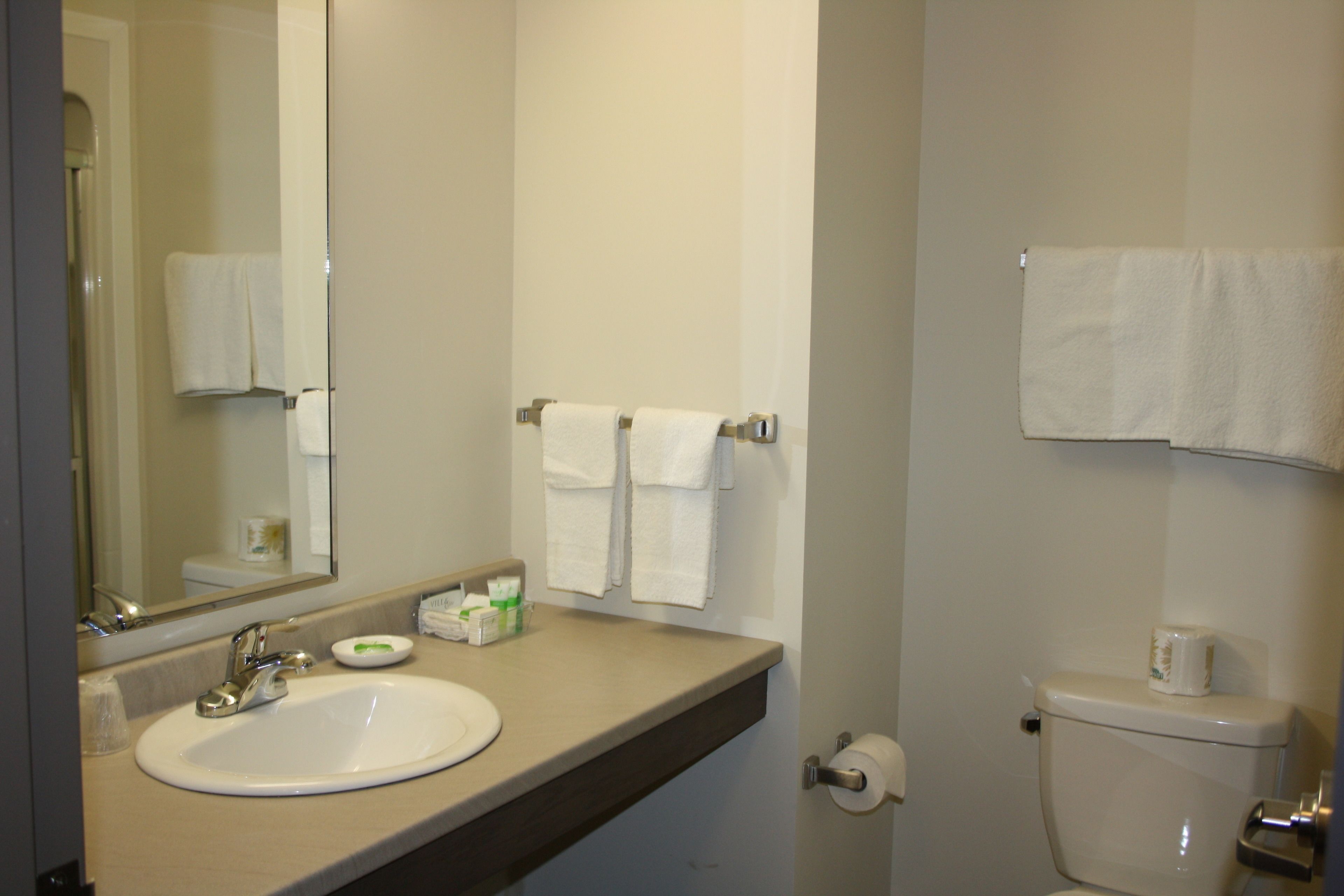 A bathroom with a sink, mirror, towel rack, toilet, and a roll of toilet paper.